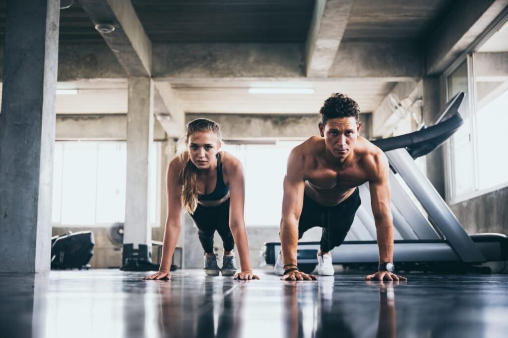 Hombre y mujer realizando flexiones de brazos mirando a la camara